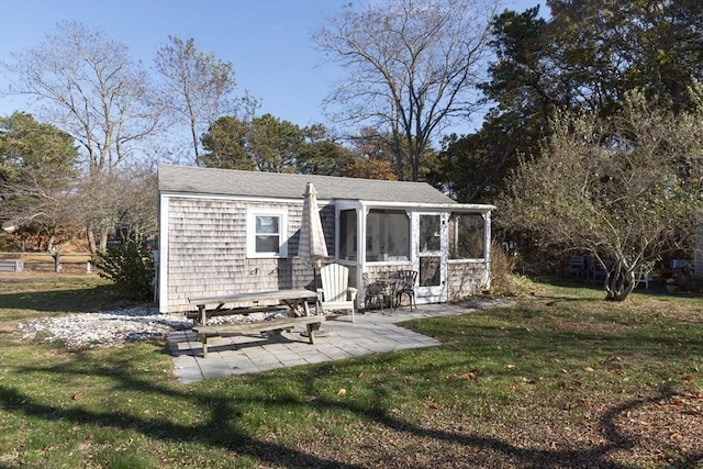 back of property with a patio area, a sunroom, a lawn, and roof with shingles