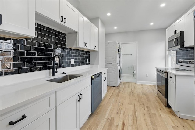 kitchen with appliances with stainless steel finishes, stacked washer / dryer, a sink, decorative backsplash, and recessed lighting