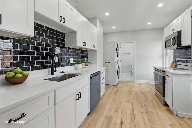 kitchen with appliances with stainless steel finishes, stacked washer / dryer, a sink, backsplash, and recessed lighting
