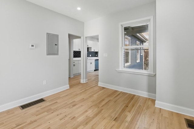 spare room featuring electric panel, baseboards, light wood-type flooring, and recessed lighting