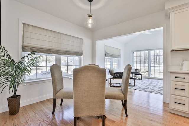 dining room featuring lofted ceiling, light wood-style flooring, baseboards, and a wealth of natural light