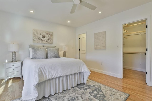 bedroom featuring recessed lighting, a walk in closet, light wood-type flooring, and baseboards