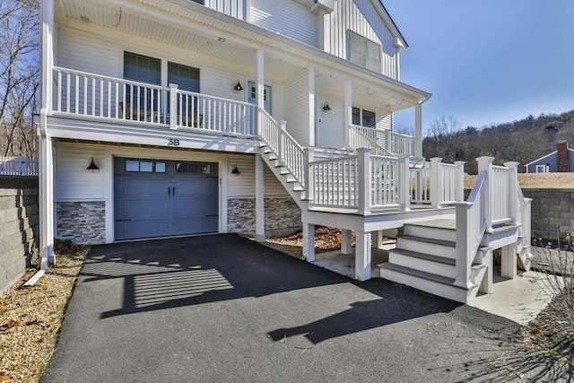 view of front of home featuring aphalt driveway, a porch, an attached garage, and stairs