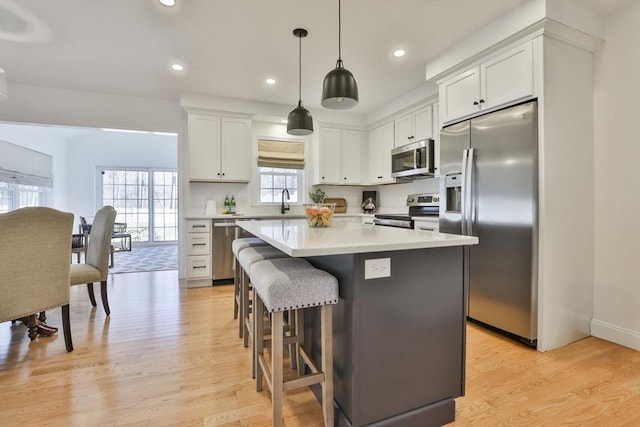 kitchen featuring a kitchen bar, a kitchen island, stainless steel appliances, light wood-style floors, and white cabinets