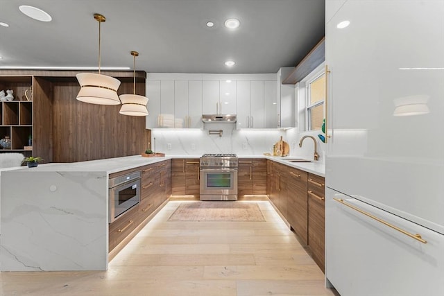 kitchen with light wood-type flooring, stainless steel appliances, sink, white cabinets, and hanging light fixtures