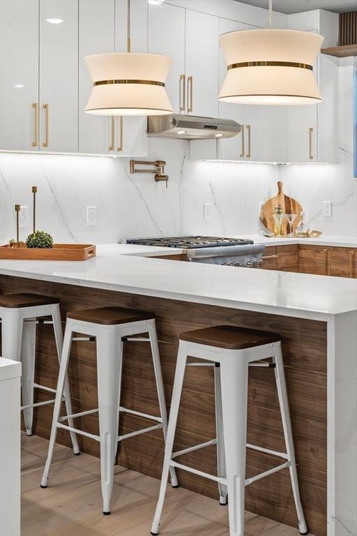 kitchen featuring white cabinetry, light hardwood / wood-style flooring, decorative backsplash, a breakfast bar, and appliances with stainless steel finishes