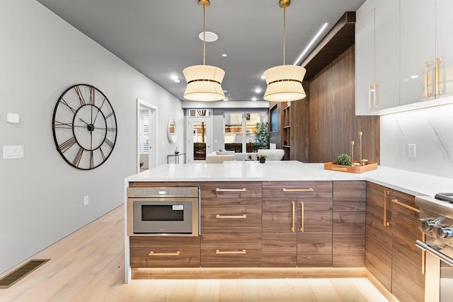 kitchen featuring pendant lighting, stainless steel appliances, white cabinetry, and light hardwood / wood-style floors