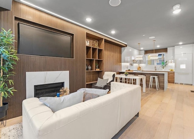 living room featuring light hardwood / wood-style floors, wooden walls, and a premium fireplace