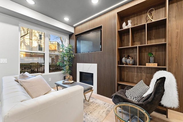 sitting room with light hardwood / wood-style flooring, wood walls, and a premium fireplace