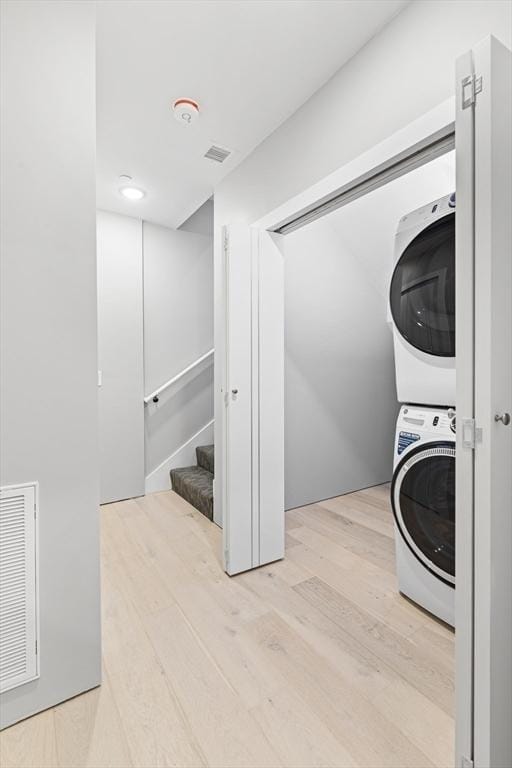 clothes washing area featuring light hardwood / wood-style flooring and stacked washer and clothes dryer