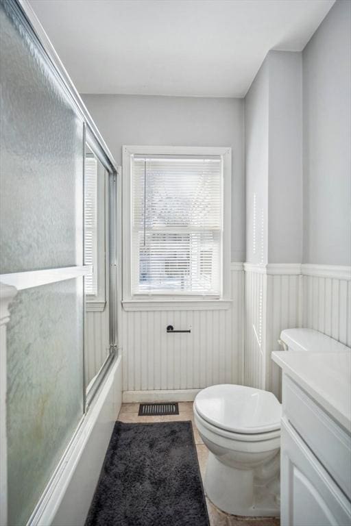 full bath featuring a wainscoted wall, visible vents, toilet, enclosed tub / shower combo, and vanity