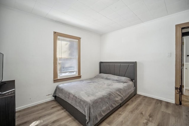 bedroom with ornamental molding, baseboards, and wood finished floors