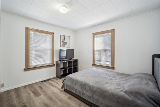 bedroom featuring baseboards, crown molding, visible vents, and wood finished floors