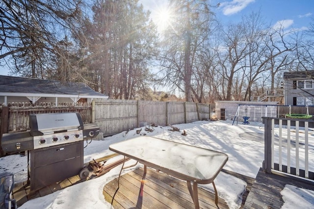 snow covered deck with outdoor dining space, a patio area, a fenced backyard, and grilling area