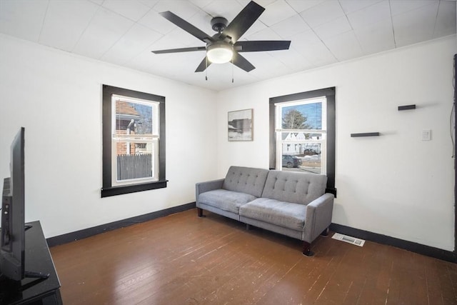 living area with a ceiling fan, baseboards, visible vents, and hardwood / wood-style floors