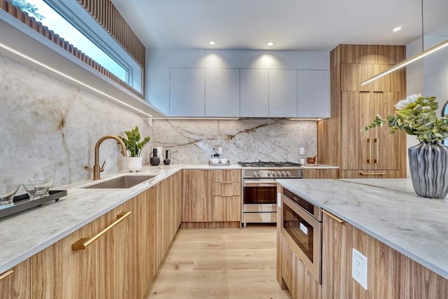 kitchen featuring sink, appliances with stainless steel finishes, light stone counters, tasteful backsplash, and light hardwood / wood-style floors