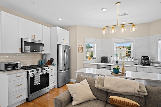 kitchen featuring hanging light fixtures, light hardwood / wood-style flooring, decorative backsplash, white cabinetry, and stainless steel appliances