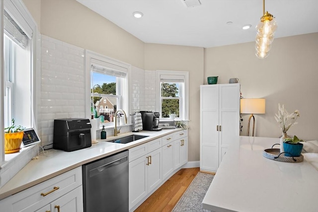 kitchen featuring white cabinetry, sink, hanging light fixtures, black dishwasher, and light wood-type flooring