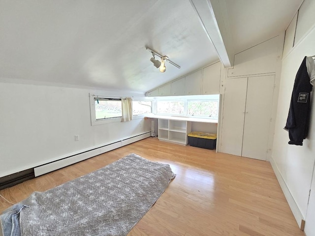 additional living space featuring a healthy amount of sunlight, light wood-style floors, vaulted ceiling, and a baseboard heating unit