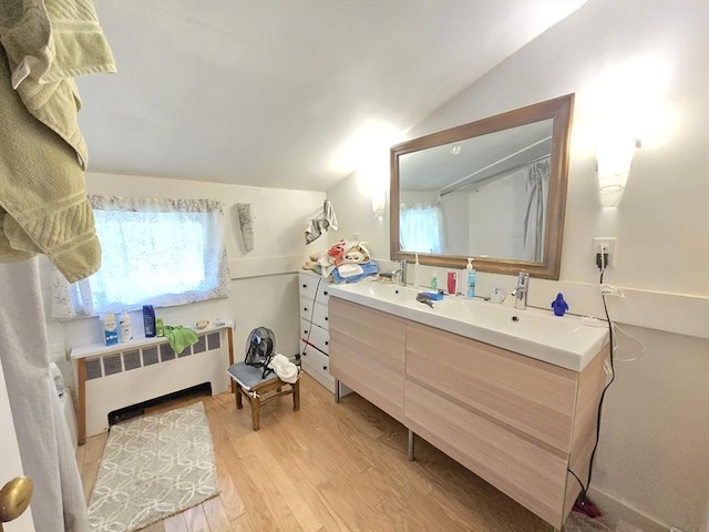 bathroom featuring double vanity, vaulted ceiling, radiator heating unit, and wood finished floors