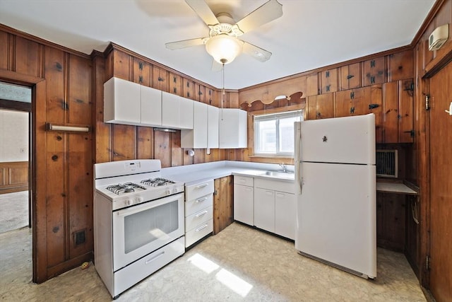 kitchen featuring a sink, wood walls, light countertops, light floors, and white appliances