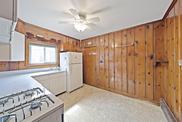 kitchen featuring white appliances, light countertops, ceiling fan, a sink, and wooden walls