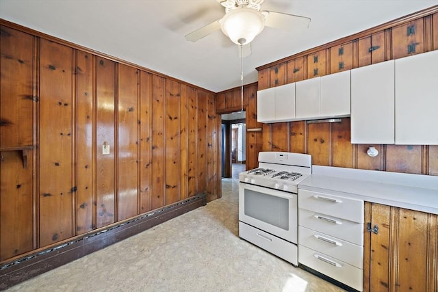 kitchen with gas range gas stove, a ceiling fan, wood walls, light countertops, and white cabinets