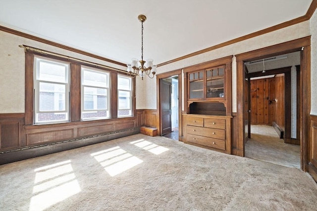 unfurnished dining area featuring a wainscoted wall, crown molding, a notable chandelier, and carpet floors