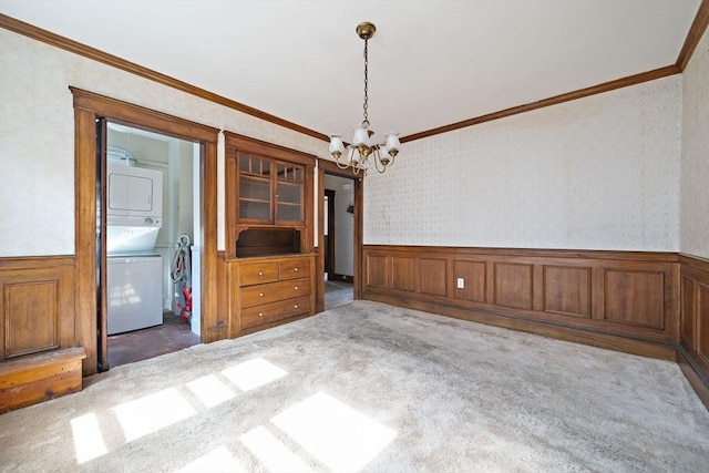 unfurnished dining area featuring stacked washer and dryer, an inviting chandelier, carpet flooring, and wainscoting