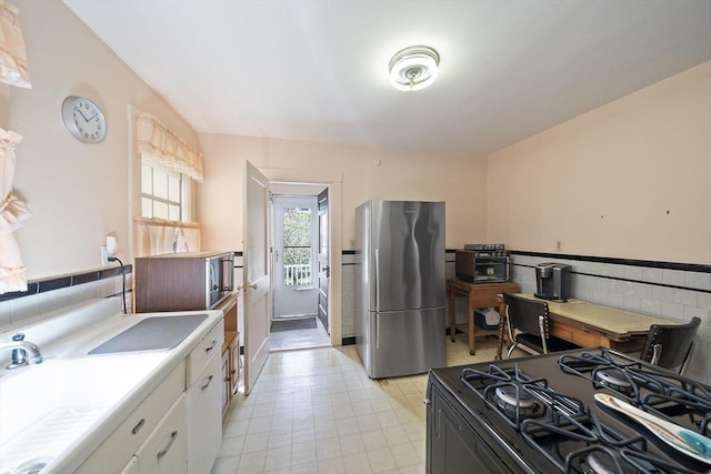 kitchen featuring black gas stove, light countertops, white cabinets, freestanding refrigerator, and light floors