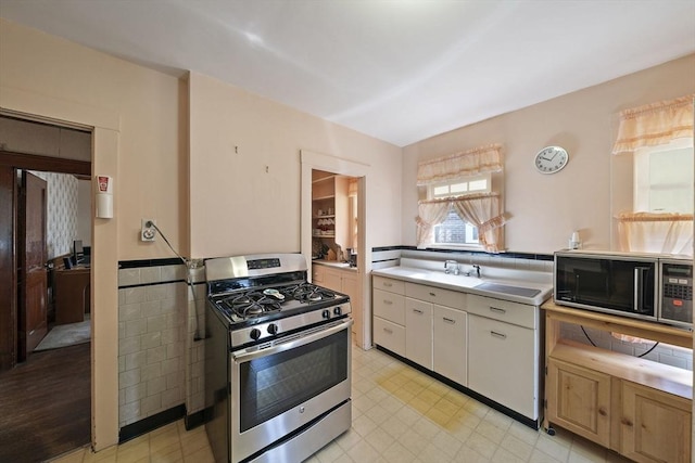 kitchen featuring light floors, stainless steel gas range oven, light countertops, white cabinetry, and black microwave