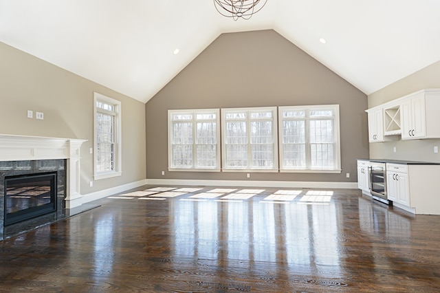 unfurnished living room with high vaulted ceiling, beverage cooler, dark hardwood / wood-style flooring, and a high end fireplace