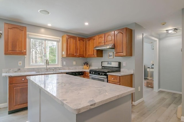 kitchen with stainless steel appliances, under cabinet range hood, a sink, light wood-style floors, and baseboards