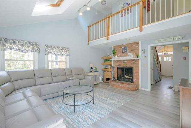 living room featuring high vaulted ceiling, wood finished floors, a skylight, rail lighting, and a fireplace