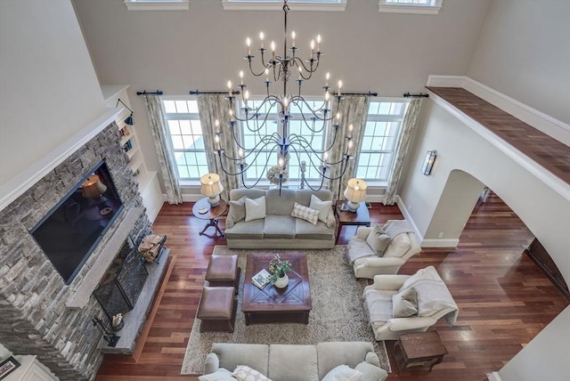 living room with a high ceiling, a stone fireplace, dark wood-type flooring, and a notable chandelier