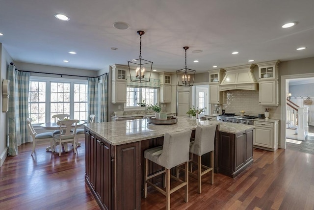 kitchen with premium range hood, a breakfast bar, light stone counters, a center island, and pendant lighting