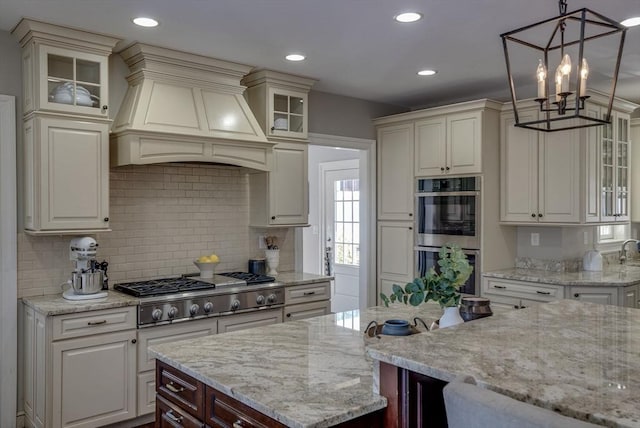 kitchen with appliances with stainless steel finishes, decorative light fixtures, light stone countertops, and wall chimney range hood