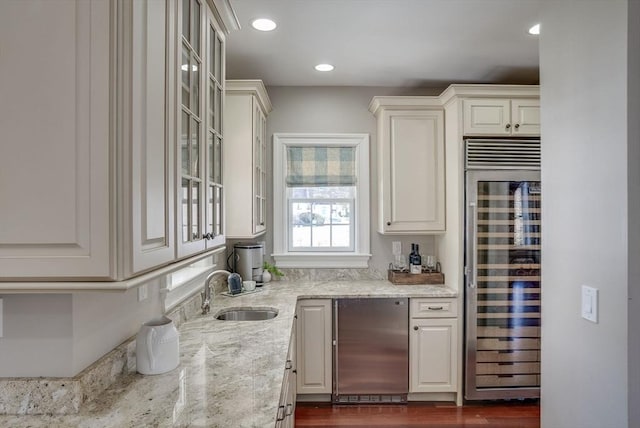 bar featuring sink, light stone counters, white cabinetry, stainless steel fridge, and beverage cooler