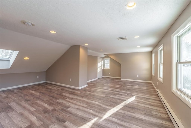 bonus room featuring hardwood / wood-style flooring, a baseboard radiator, lofted ceiling with skylight, and a textured ceiling