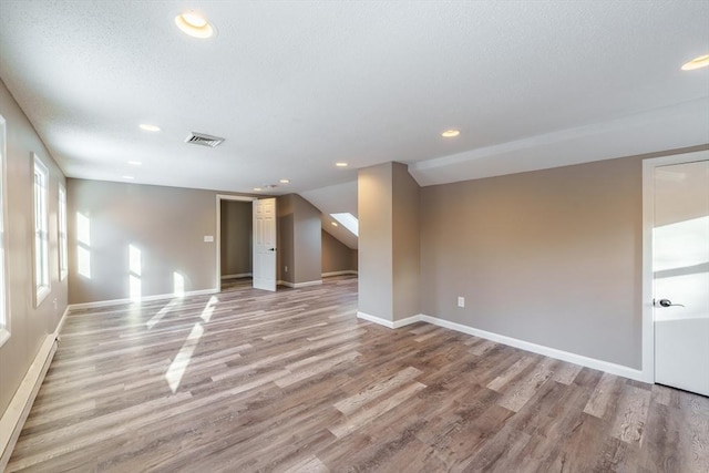 empty room featuring baseboard heating, light hardwood / wood-style floors, and a textured ceiling