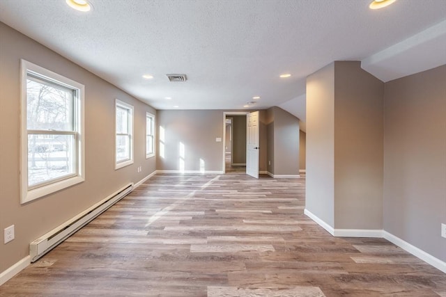 unfurnished room with a baseboard heating unit, light hardwood / wood-style flooring, a textured ceiling, and vaulted ceiling