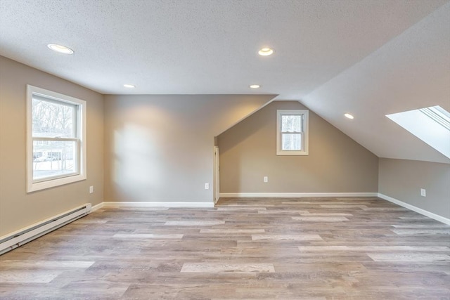 additional living space featuring baseboard heating, vaulted ceiling, light hardwood / wood-style flooring, and a textured ceiling