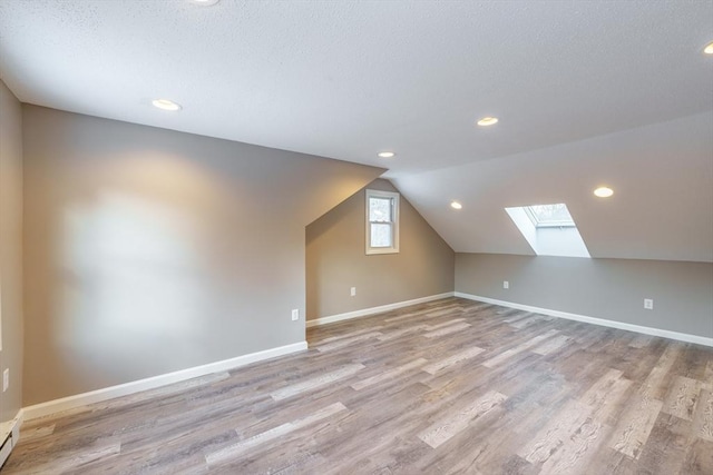 bonus room featuring vaulted ceiling with skylight, a textured ceiling, and light hardwood / wood-style floors