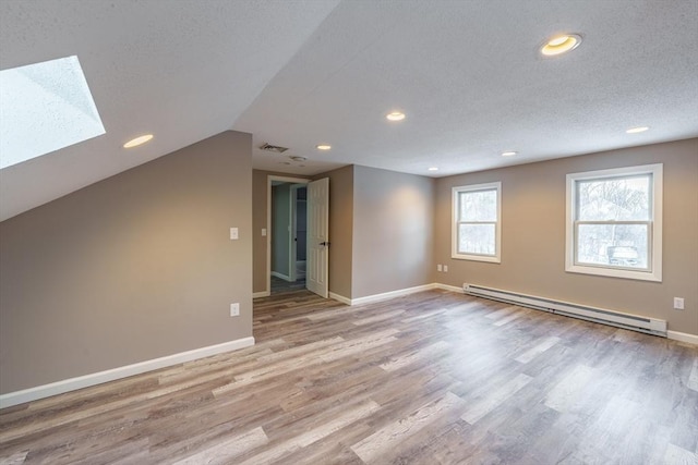 bonus room with a baseboard heating unit, a textured ceiling, light hardwood / wood-style flooring, and vaulted ceiling with skylight