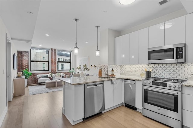 121 Portland St Unit 601, Boston, MA 02114 - kitchen featuring appliances with stainless steel finishes, white cabinets, a peninsula, decorative backsplash, and light wood-style floors