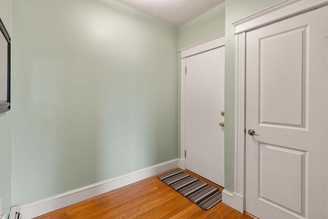 doorway featuring wood finished floors, baseboard heating, and baseboards