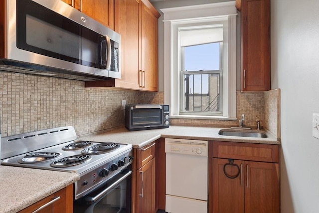 kitchen featuring stainless steel microwave, dishwasher, electric range, a sink, and brown cabinetry