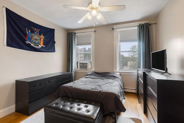 bedroom with a baseboard radiator, light wood-style flooring, cooling unit, a ceiling fan, and baseboards