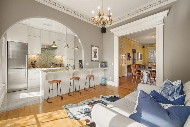 living room featuring arched walkways, crown molding, a chandelier, and light wood-type flooring