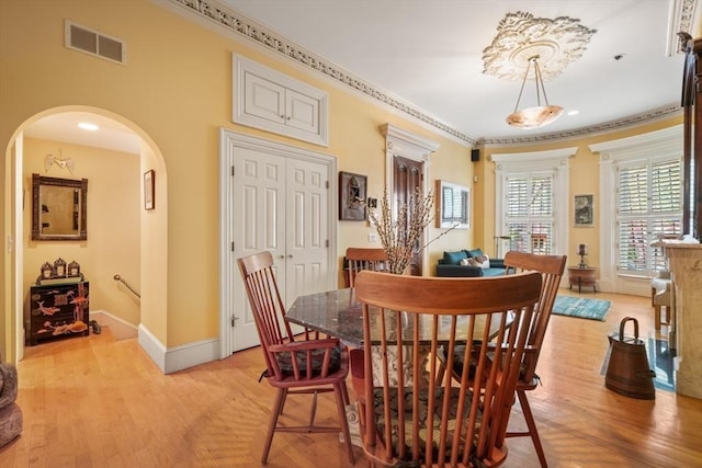 dining area with visible vents, light wood-style flooring, baseboards, and arched walkways